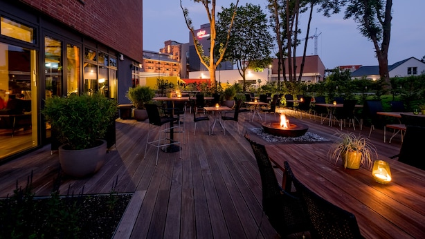 An outdoor patio with wooden tables and chairs, a fire pit, and potted plants. - FREIgeist Einbeck - A Member of Design Hotels™ (Einbeck)