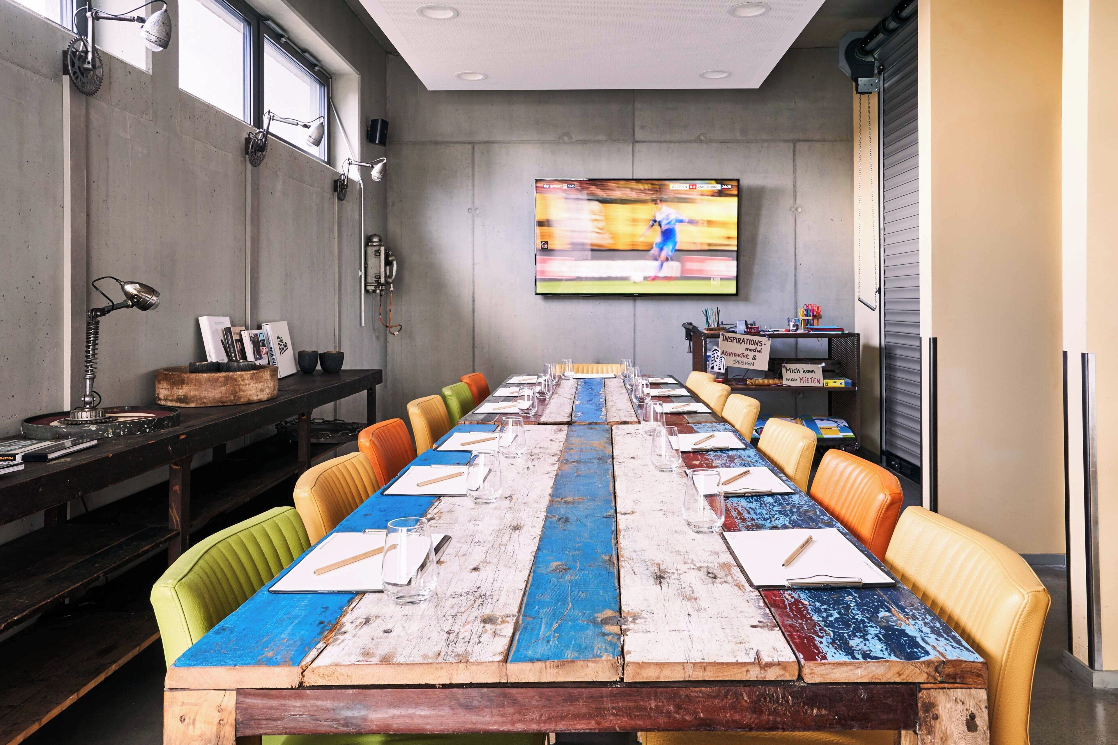 A conference room with a long table, chairs, a television, and a window.