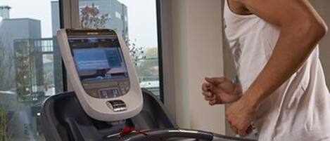 A man running on a treadmill in a gym with a digital display and a window with a city view.