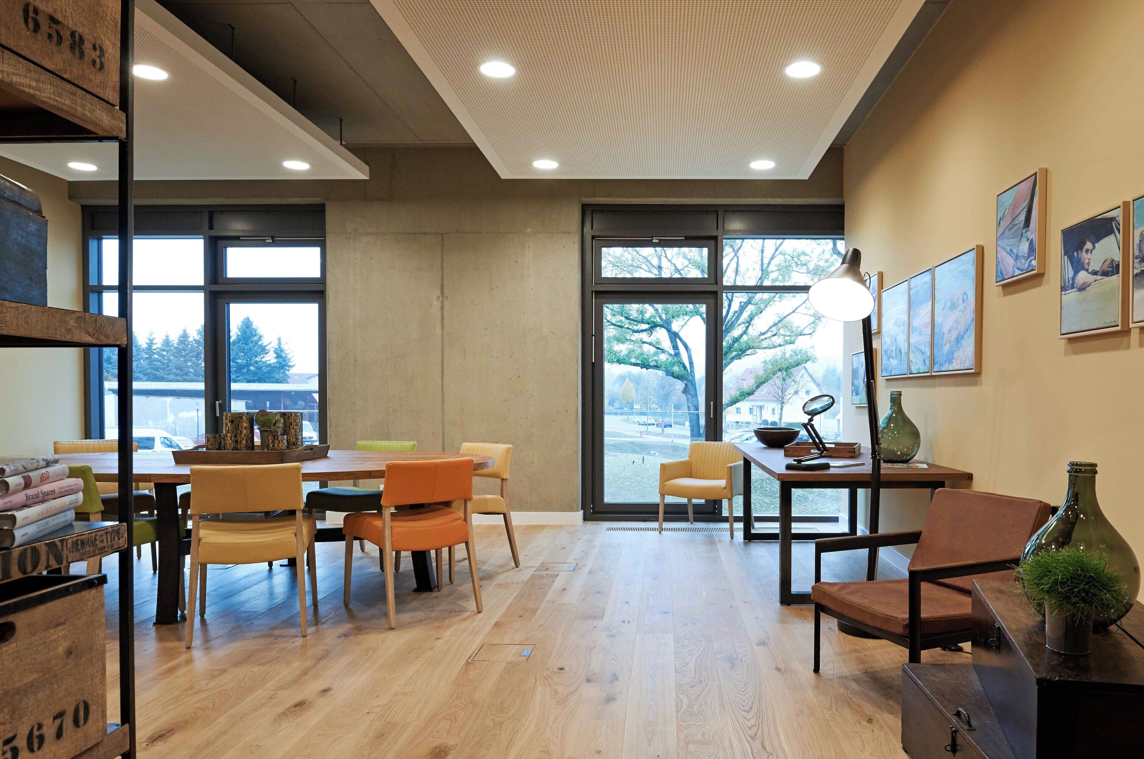 A modern interior with a wooden floor, a dining area with chairs and a table, a large window with a view, and artwork on the walls.