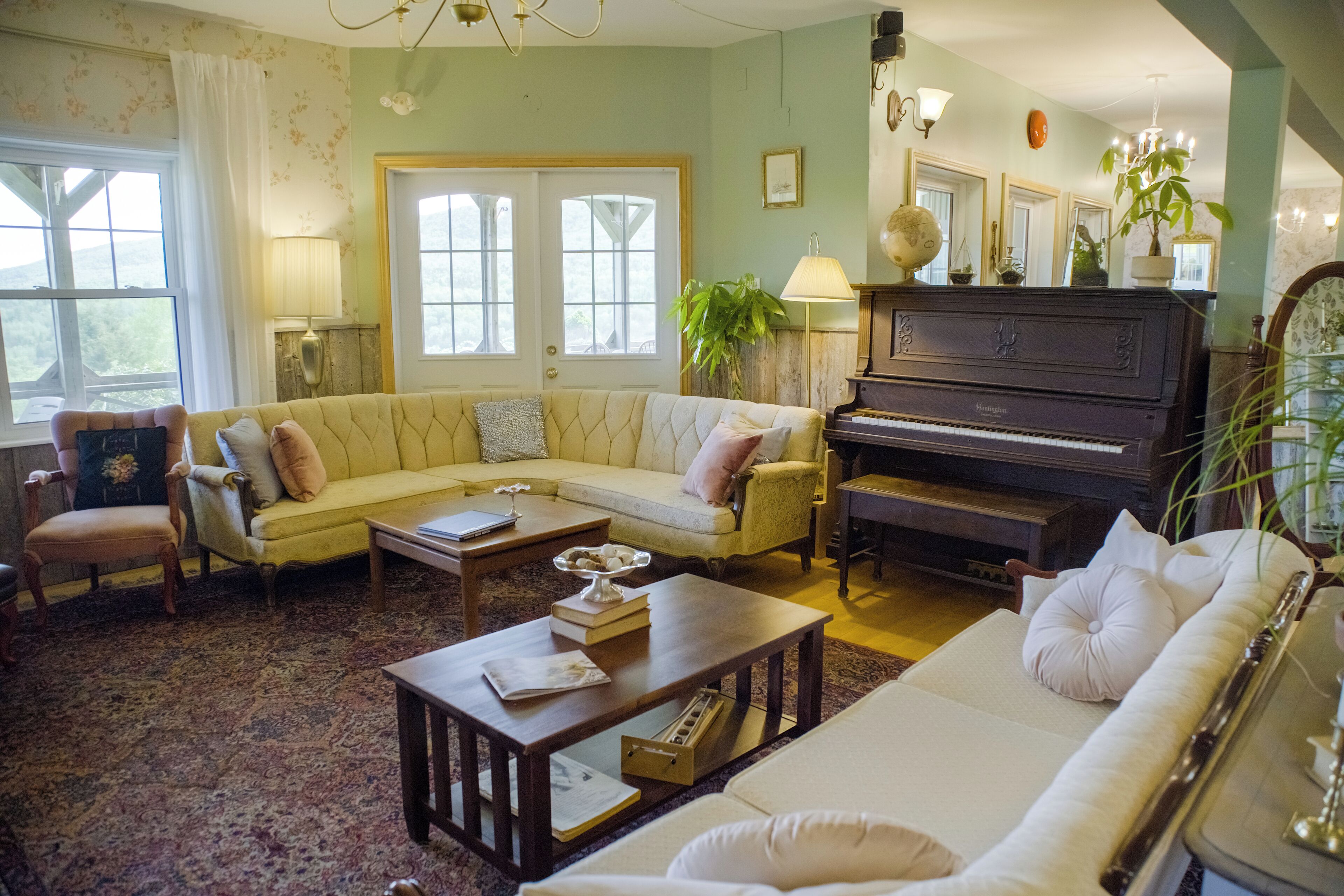 Una sala de estar con sofá, sillones, un piano y un amplio ventanal.