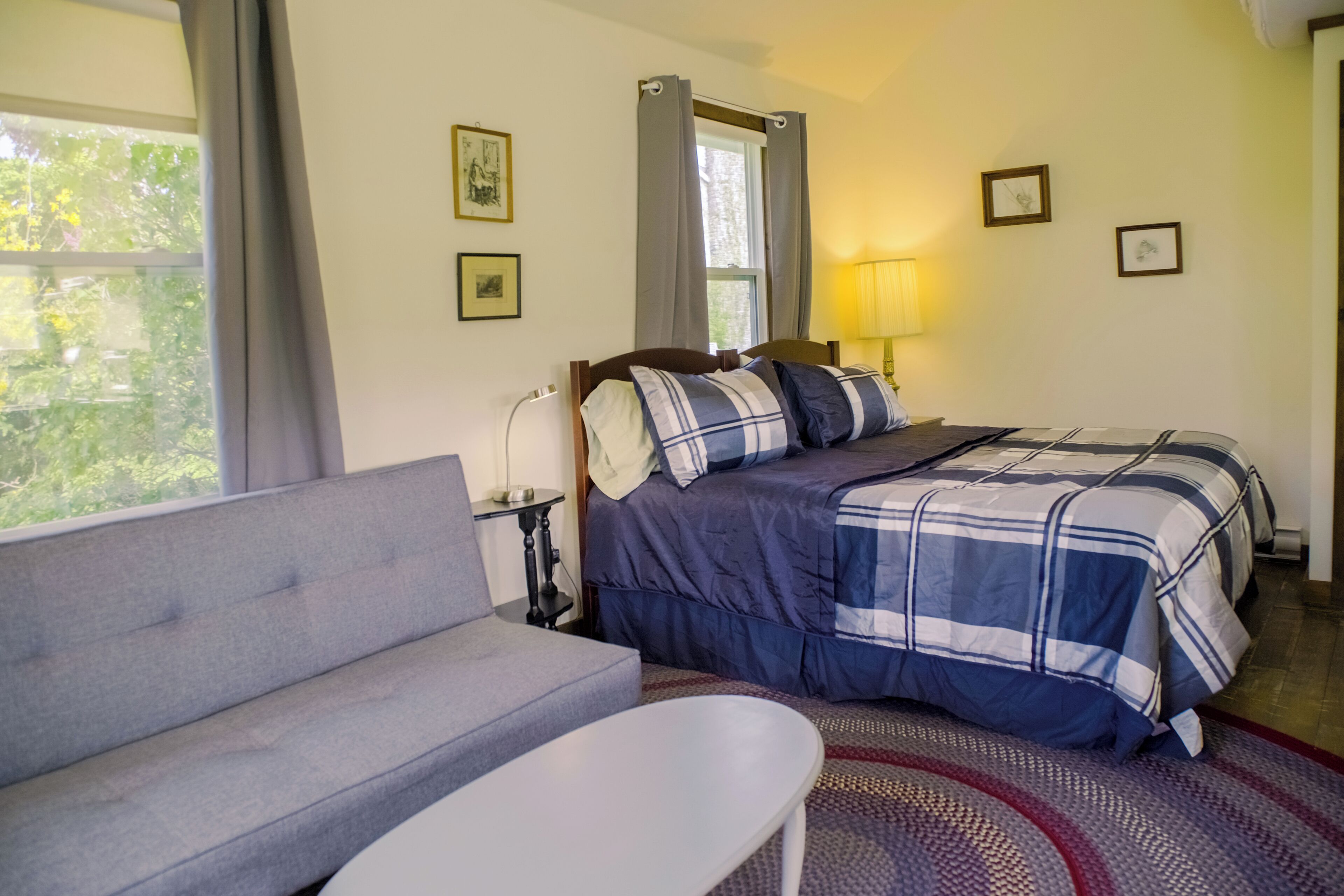 Un dormitorio con cama, sofá, mesita de noche, lámpara y cuadros en la pared.