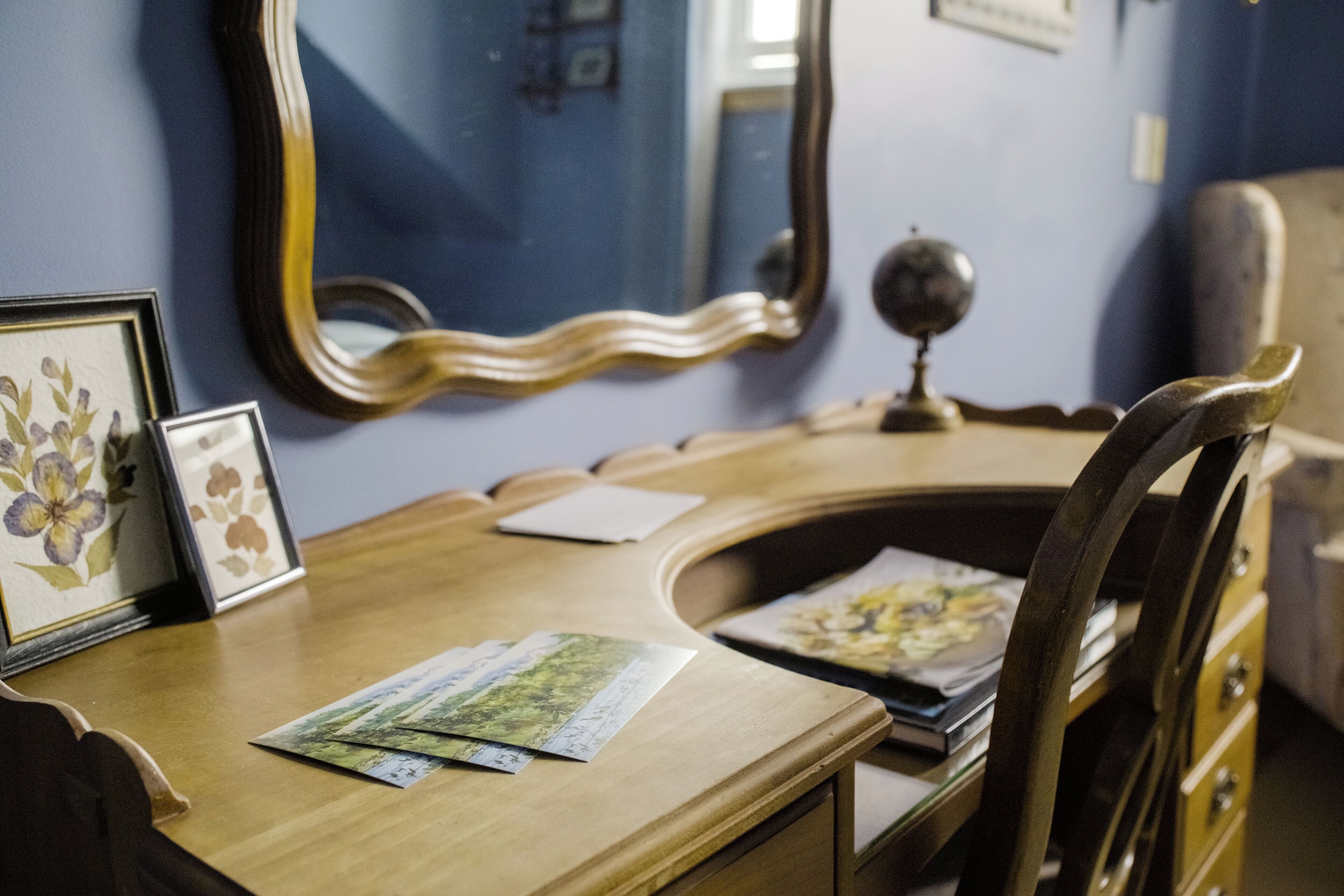 A wooden desk with framed pictures and papers, a globe, and a mirror on a blue wall.