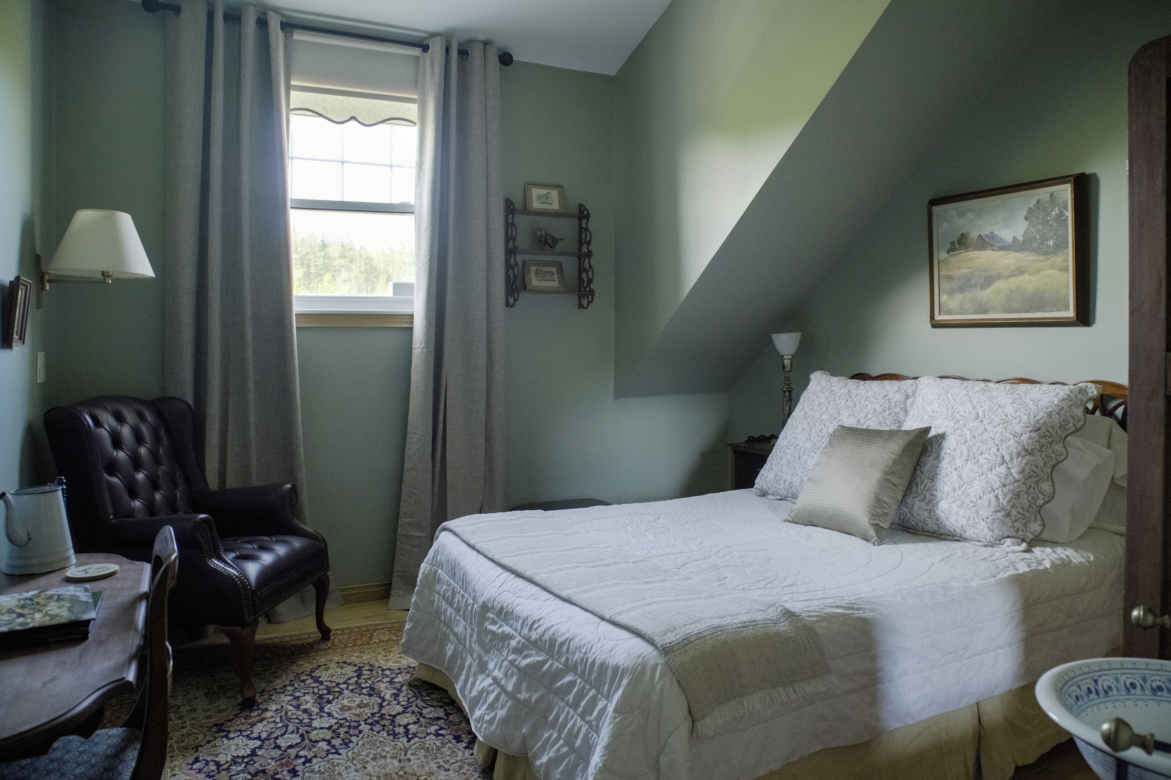A bedroom with a bed, a chair, a table, and a window with curtains.
