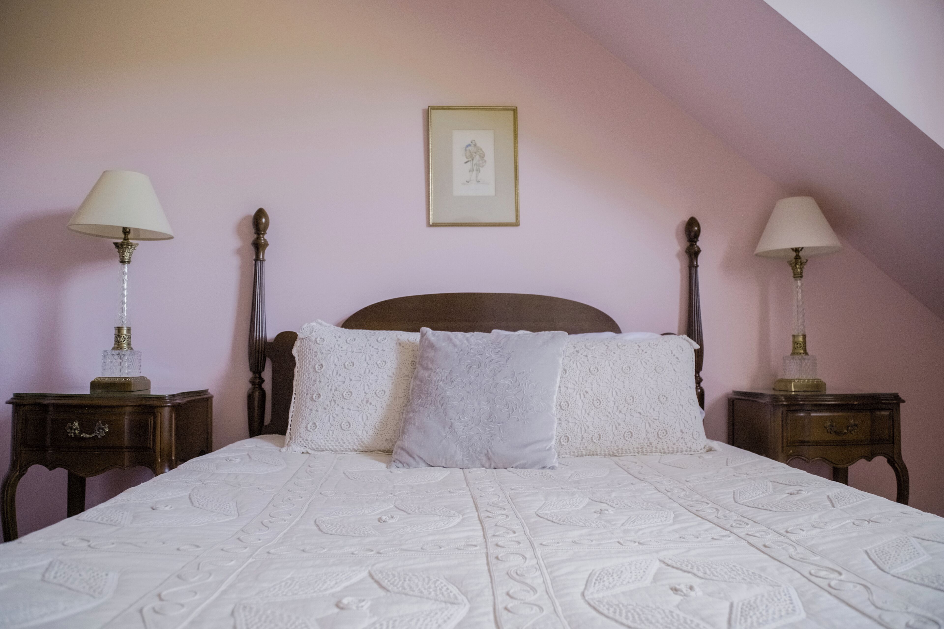 A bedroom with a large bed, two nightstands, a framed picture on the wall, and a sloped ceiling.