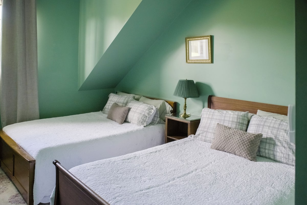 A bedroom with two single beds, a nightstand with a lamp, and a framed picture on the wall.