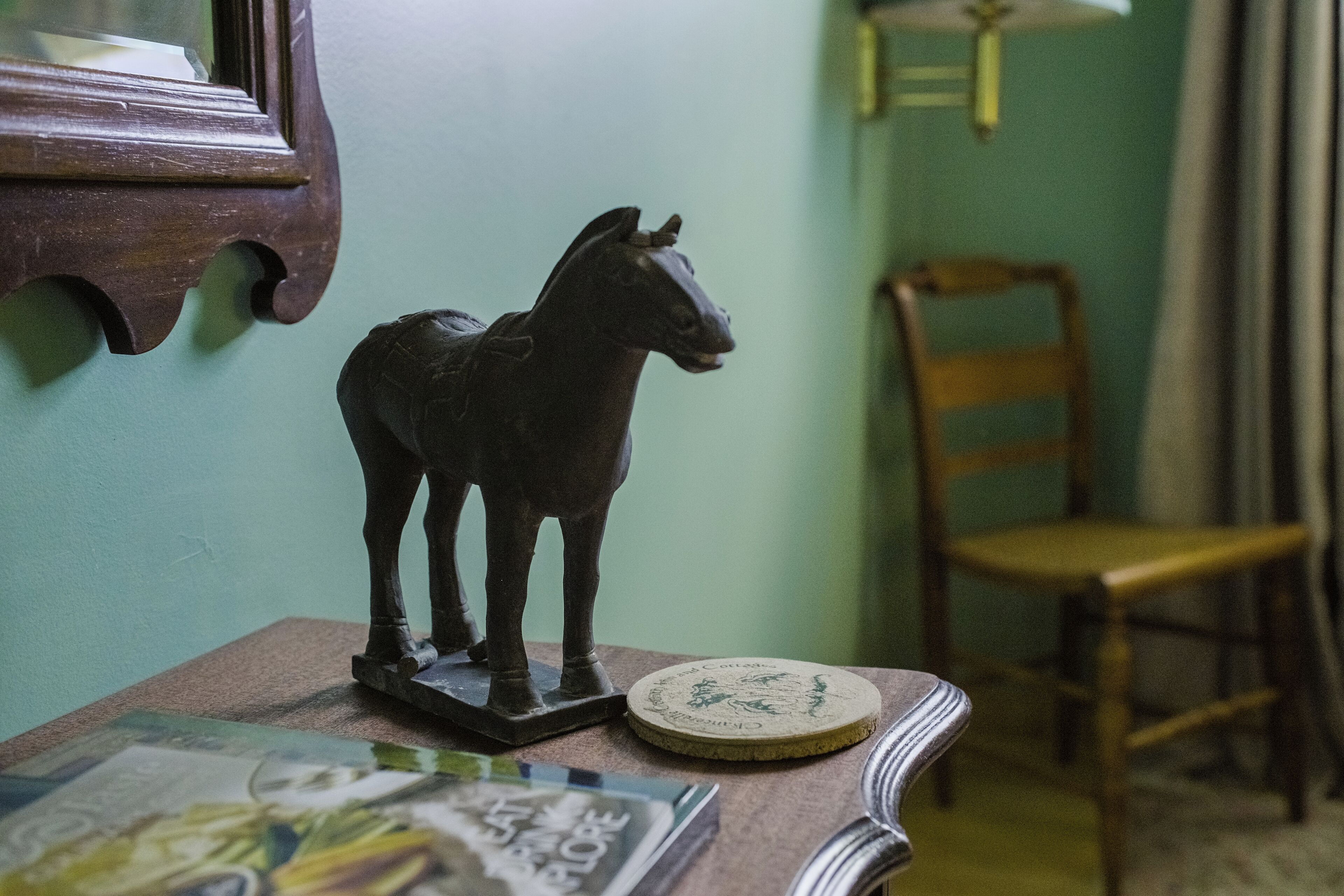 A wooden horse figurine on a table, a chair, and a framed mirror on the wall.