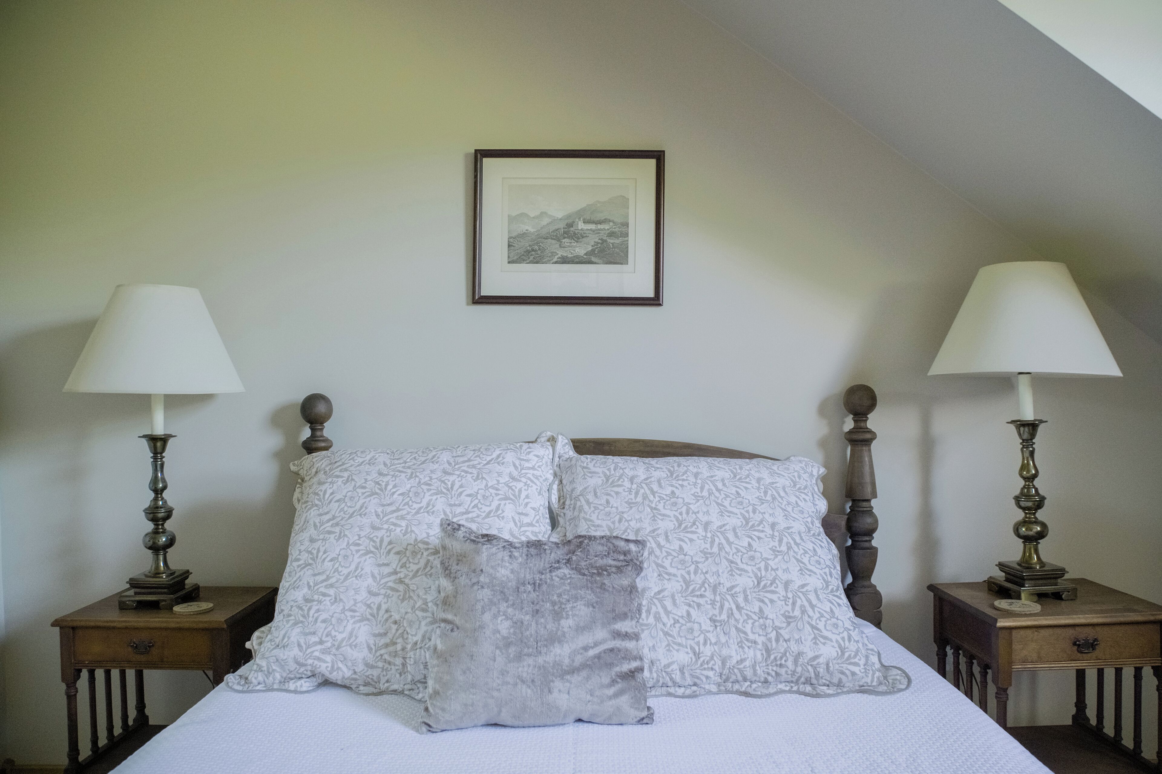 A neatly made bed with patterned pillows, two bedside tables with lamps, and a framed picture on the wall.