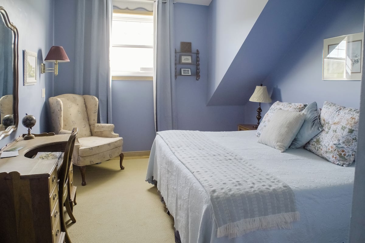 A bedroom with a bed, a chair, a desk, and a lamp.
