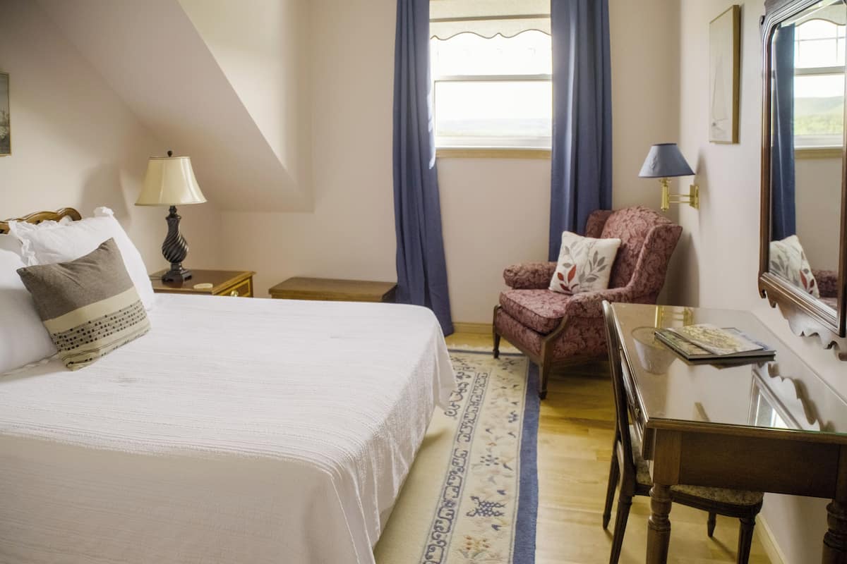 A bedroom with a bed, a chair, a desk, and a window with curtains.