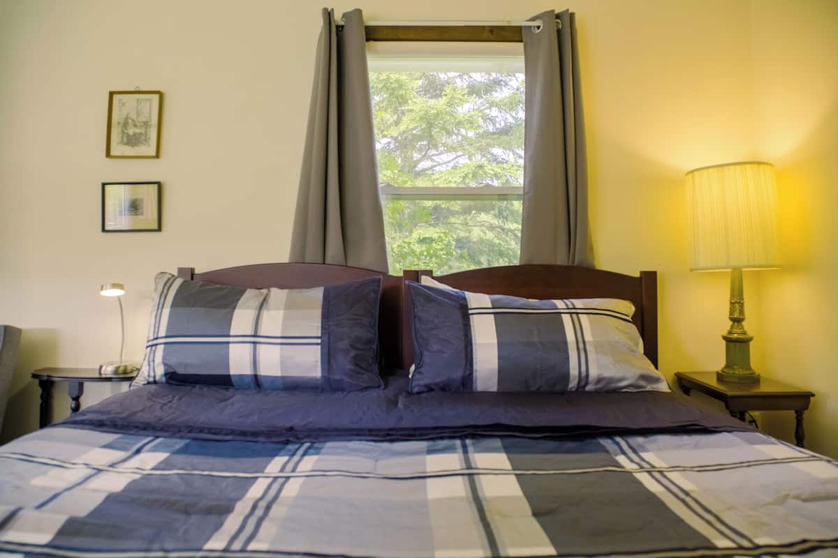 A bed with a plaid bedspread, a nightstand with a lamp, and a window with curtains.