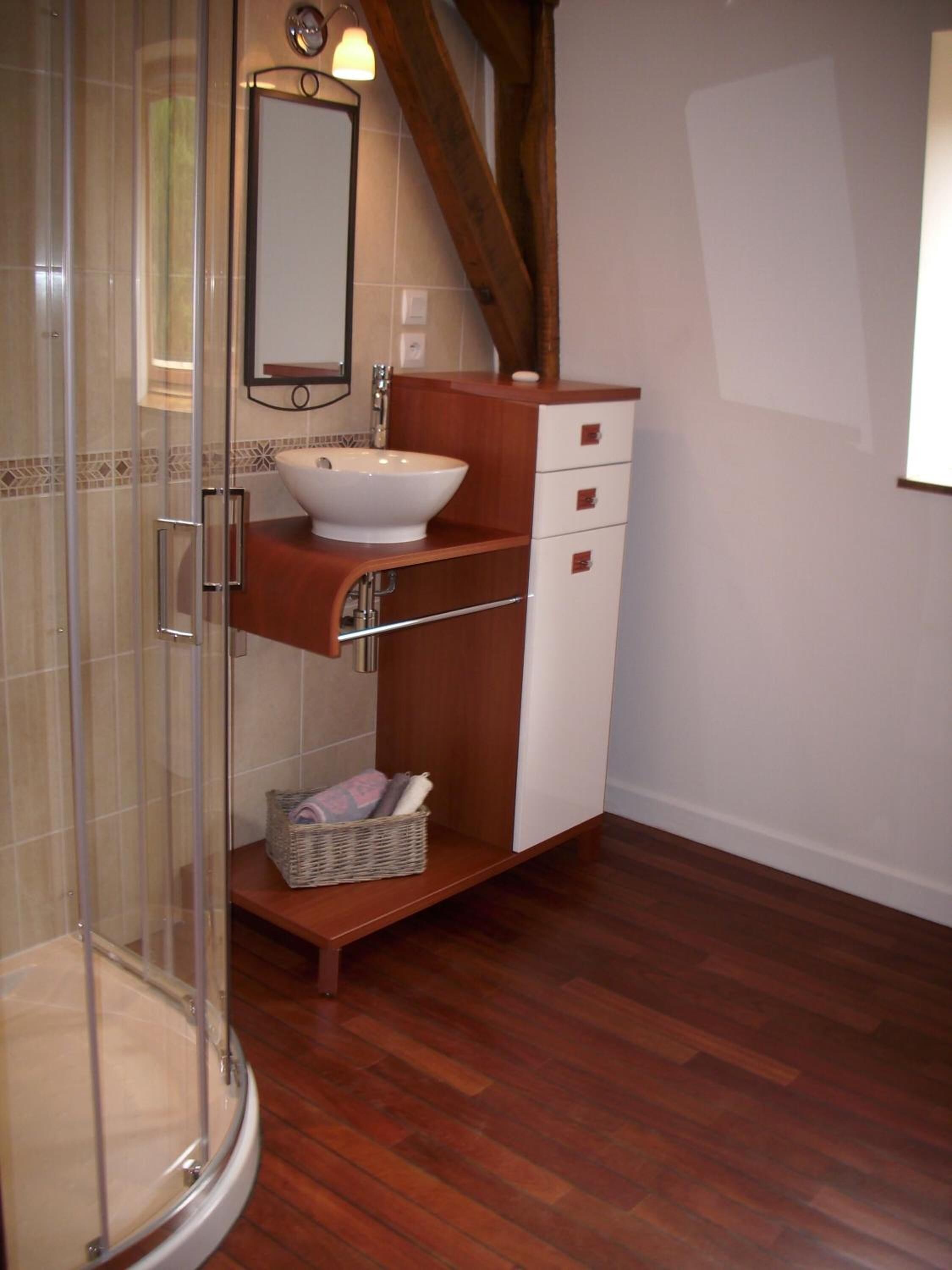 A bathroom with a glass shower enclosure, a white sink, wooden cabinetry, and a mirror.