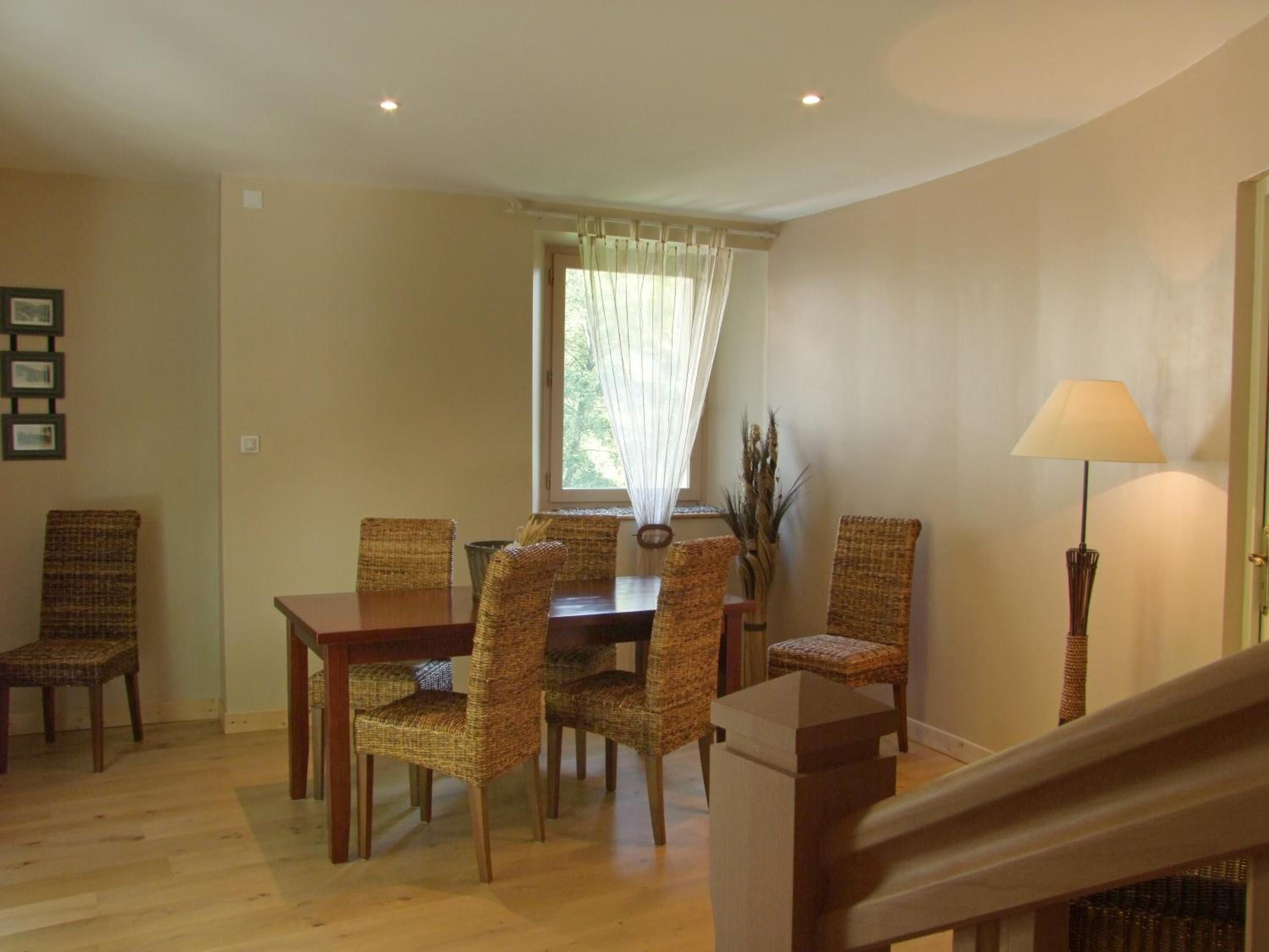 Un comedor con mesa de madera y sillas de mimbre, una ventana con cortinas y una lámpara en pie.