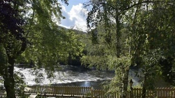 A serene outdoor area with a wooden bench, a stone table, and a river.