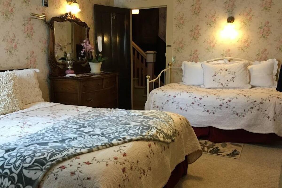 A bedroom with two beds, a dresser, a mirror, and a staircase.