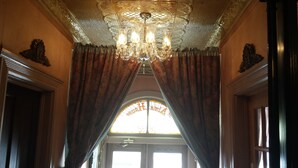Una habitación ornamentada con un candelabro, cortinas con drapeados y un ventanal con vitrales.