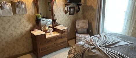 A bedroom with a large bed, a dresser with a mirror, a chair, a television on a stand, and a window with curtains.