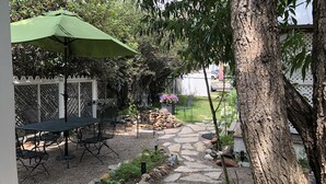 Un patio con mesa y sillas, un parasol verde y un camino de piedra.