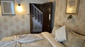 Un dormitorio con papel tapiz floral, una cama con manta decorativa, un cuadro enmarcado y una escalera.