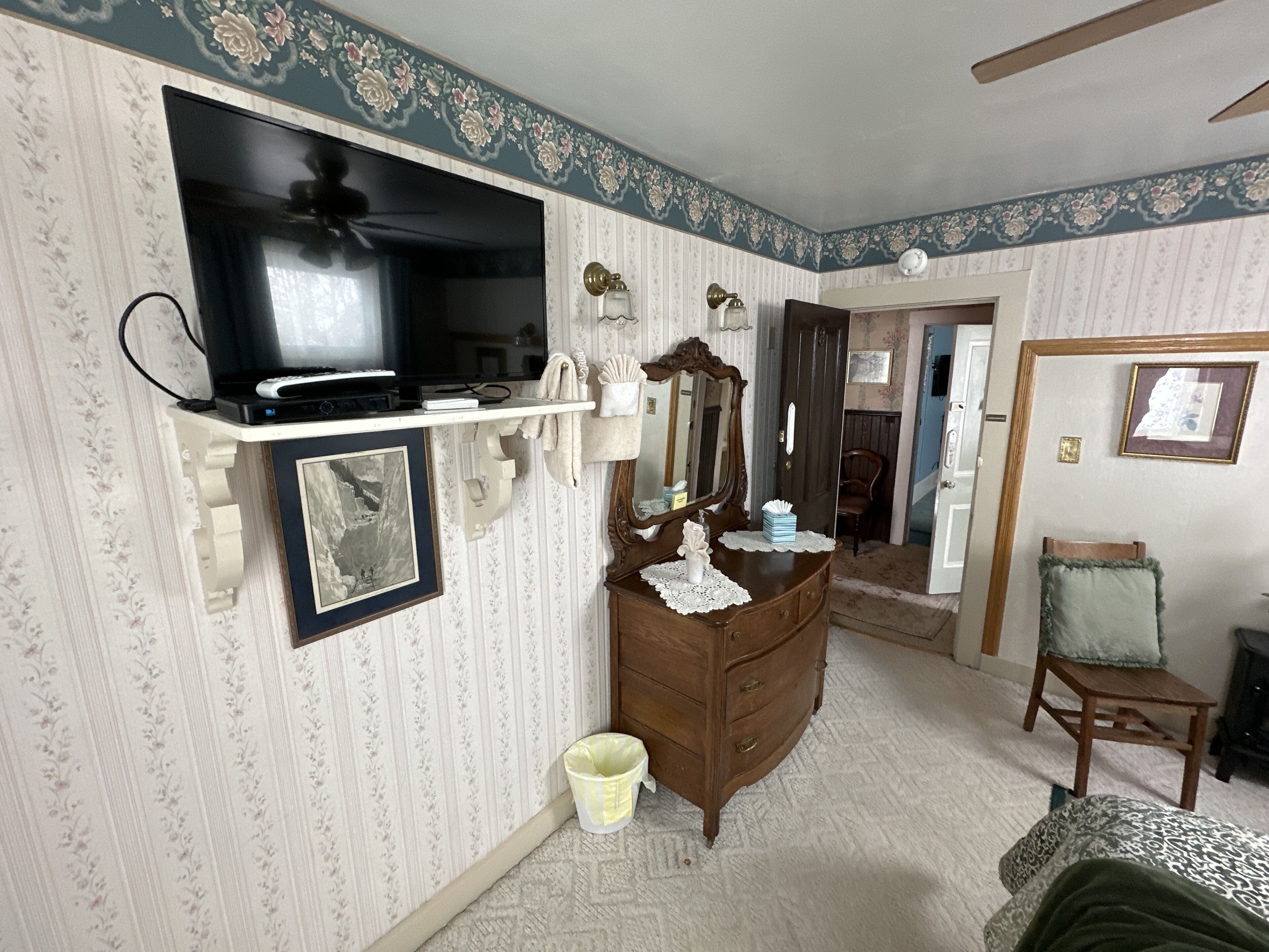 Un dormitorio con un aparador, televisión, espejo y una silla.