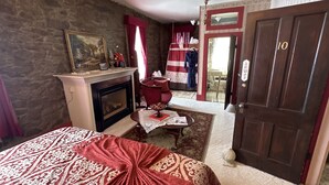 Una habitación con chimenea, una cama con colcha de cuadros rojos y blancos, una mesita con un periódico y una puerta con el número 10.