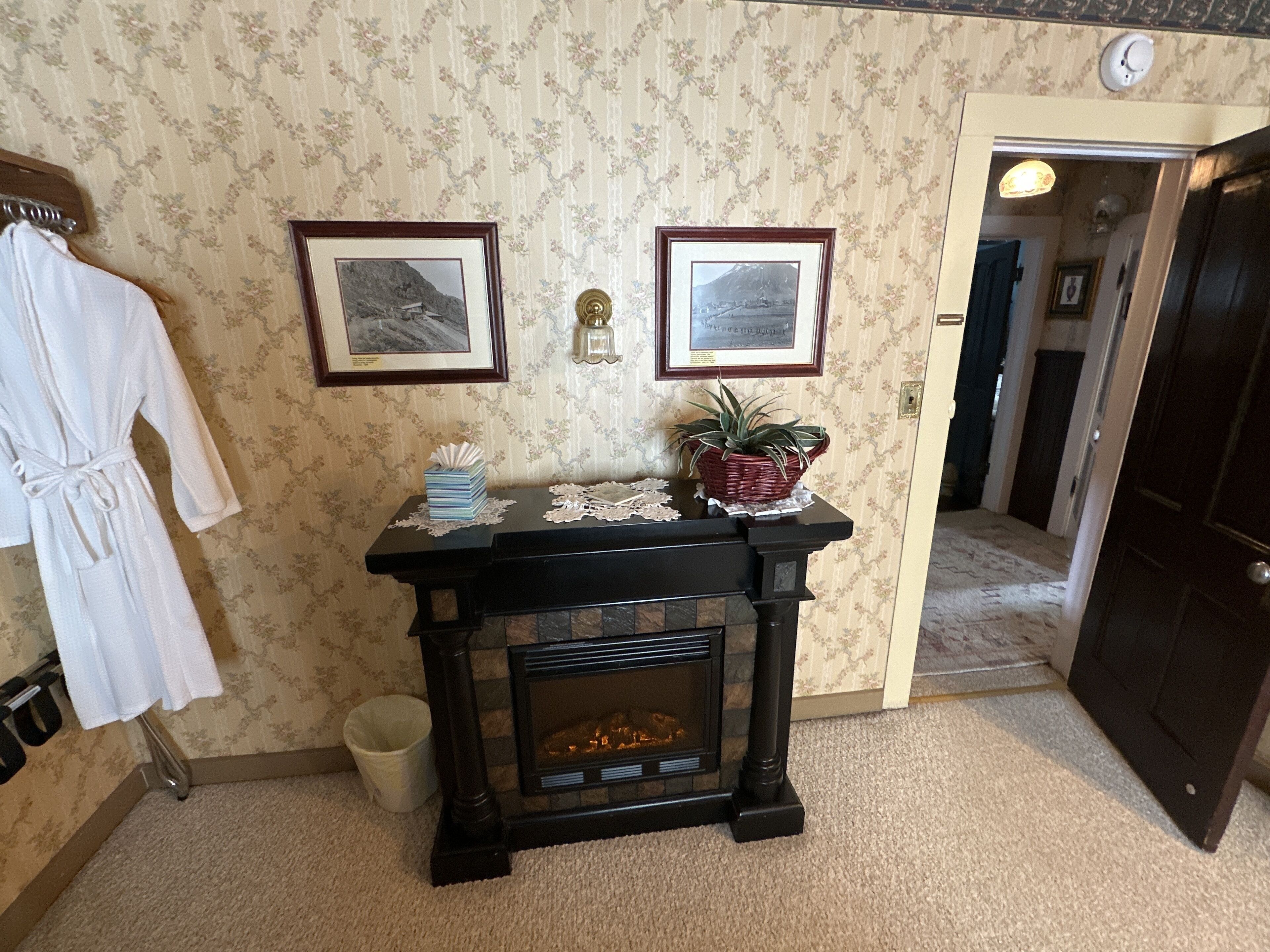 A room with a fireplace, a white robe hanging, and two framed pictures on the wall.