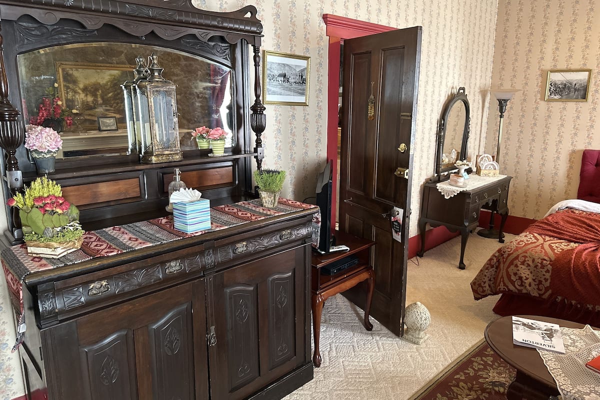 A room with a wooden dresser, a mirror, a bed, and a door.