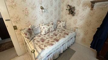A small, cozy bedroom with floral wallpaper, a single bed with a white frame, and a wooden door.