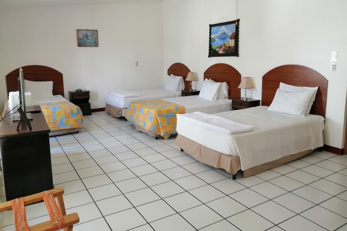 Une chambre d’hôtel avec trois lits, un bureau avec un ordinateur et une télévision.