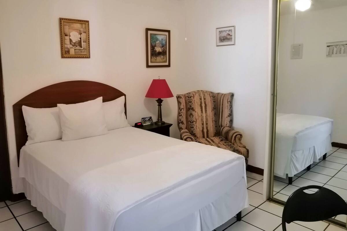 Une chambre d’hôtel avec un lit, une chaise, une lampe et un miroir.
