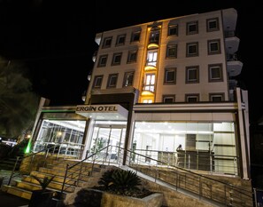 A hotel with a sign reading "ERGİN OTEL" at the entrance, featuring a modern design with a glass facade and a staircase leading to the entrance.