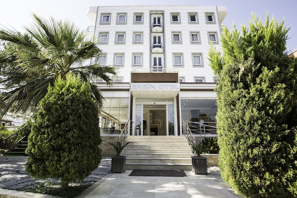 A modern hotel entrance with a staircase leading to the door, surrounded by well-maintained landscaping and a clear sky.