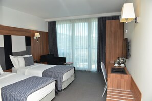 A hotel room with two beds, a desk, a chair, a TV, and a window with curtains. - Lova Hotel SPA (Yalova)