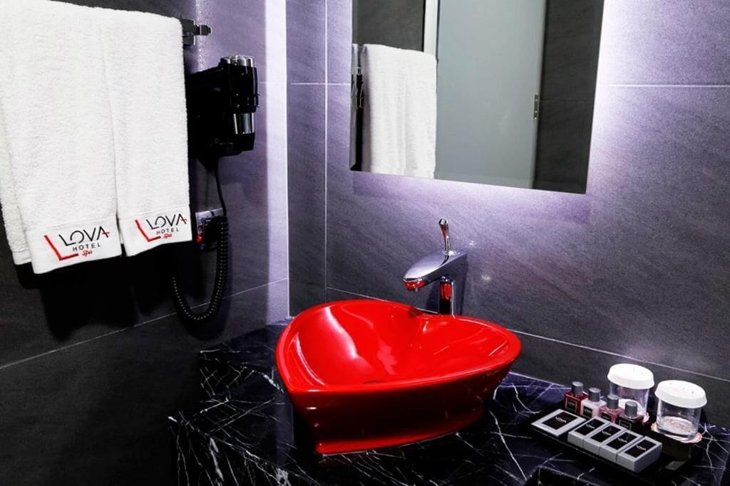 Un bany modern amb un rentapeus en forma de cor vermell, un telèfon negre i productes de tocador sobre una safata.