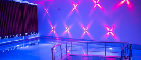 Área de piscina com design moderno, apresentando grade de metal e parede com padrões em X iluminados.
