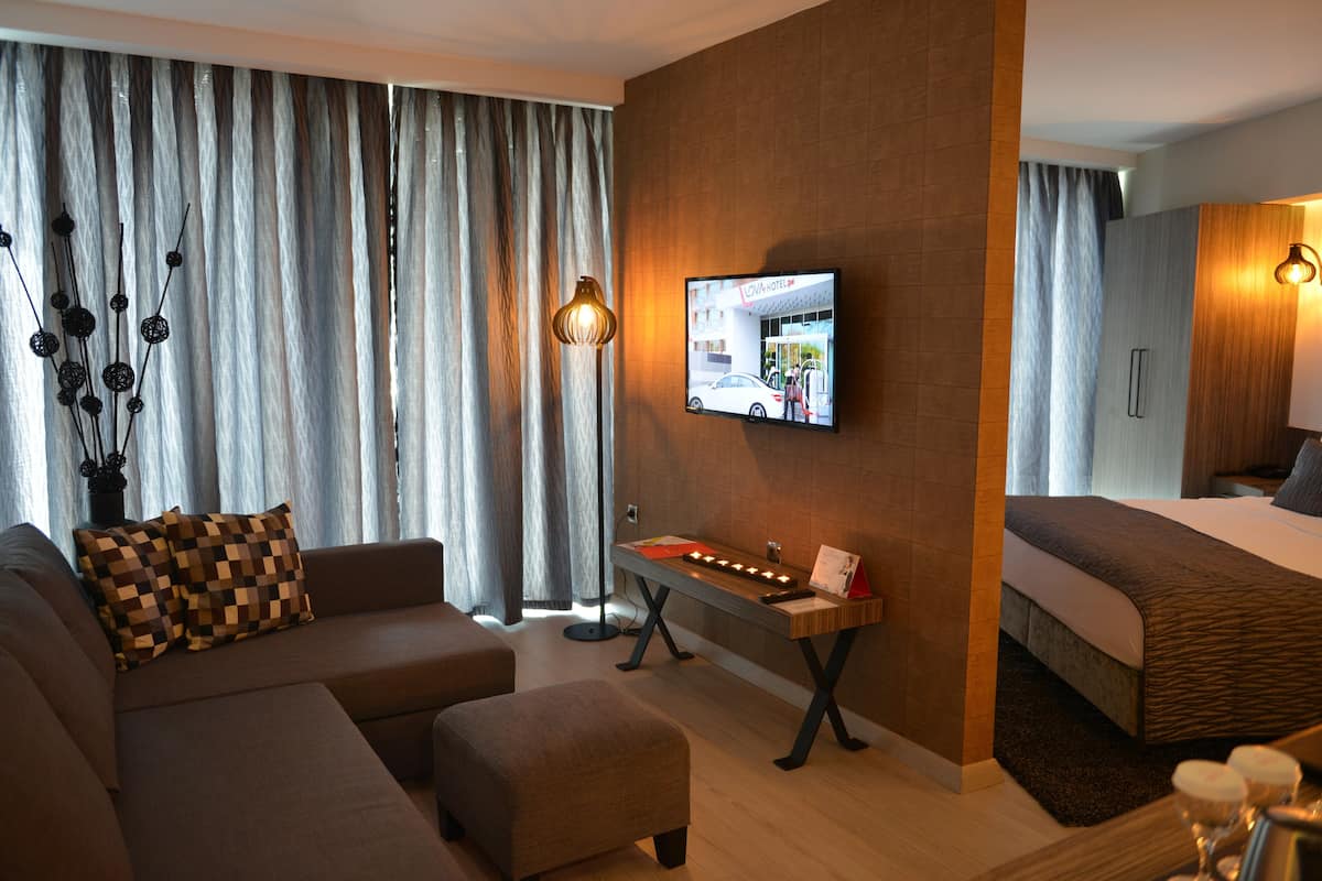 A modern hotel room with a sofa, ottoman, flat-screen TV, bedside table, and a bed.