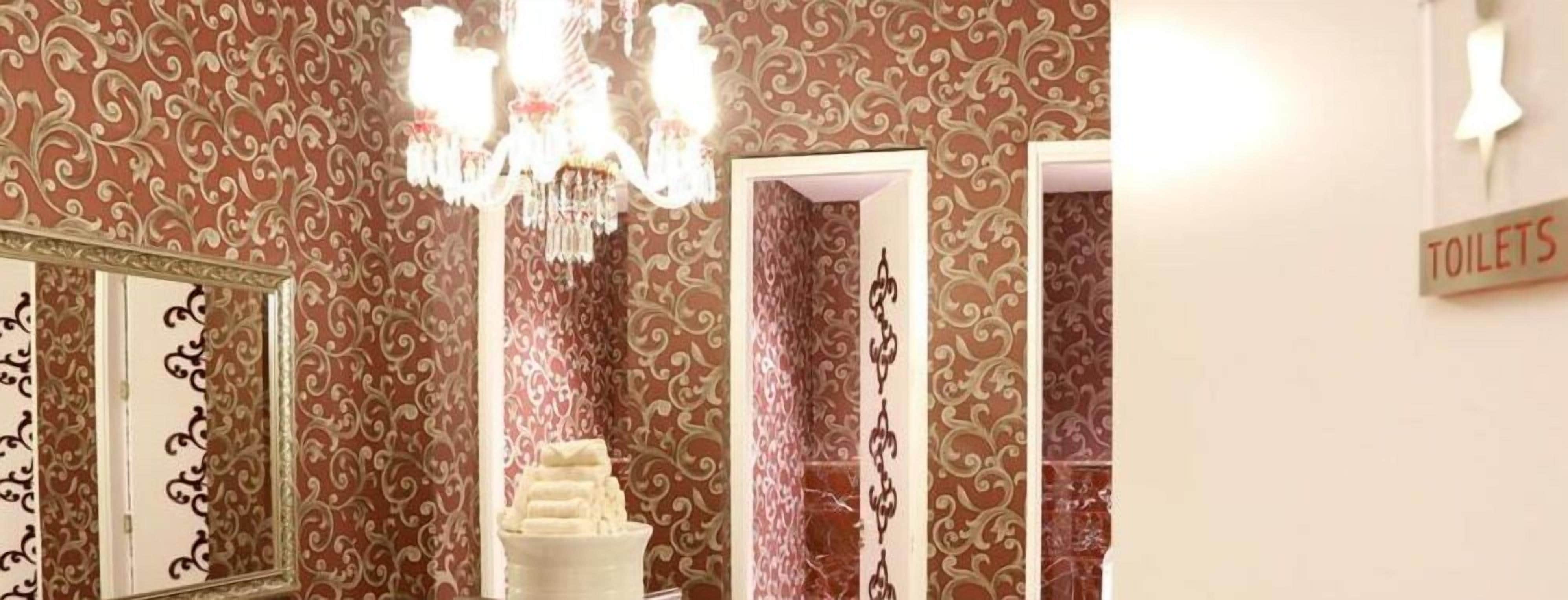 A bathroom with ornate wallpaper, a chandelier, a mirror, and a sign indicating the location of toilets.