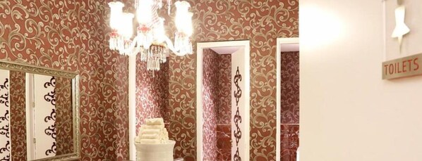 A bathroom with ornate wallpaper, a chandelier, a mirror, and a sign indicating the location of toilets. - Lova Hotel SPA (Yalova)