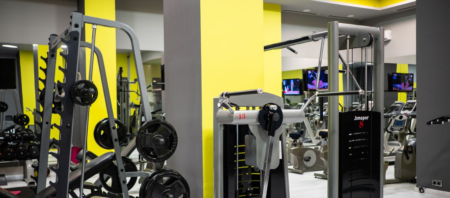 Un gimnasio con equipamiento de levantamiento de pesas variado, que incluye una estructura para sentadillas y una prensa de banca.