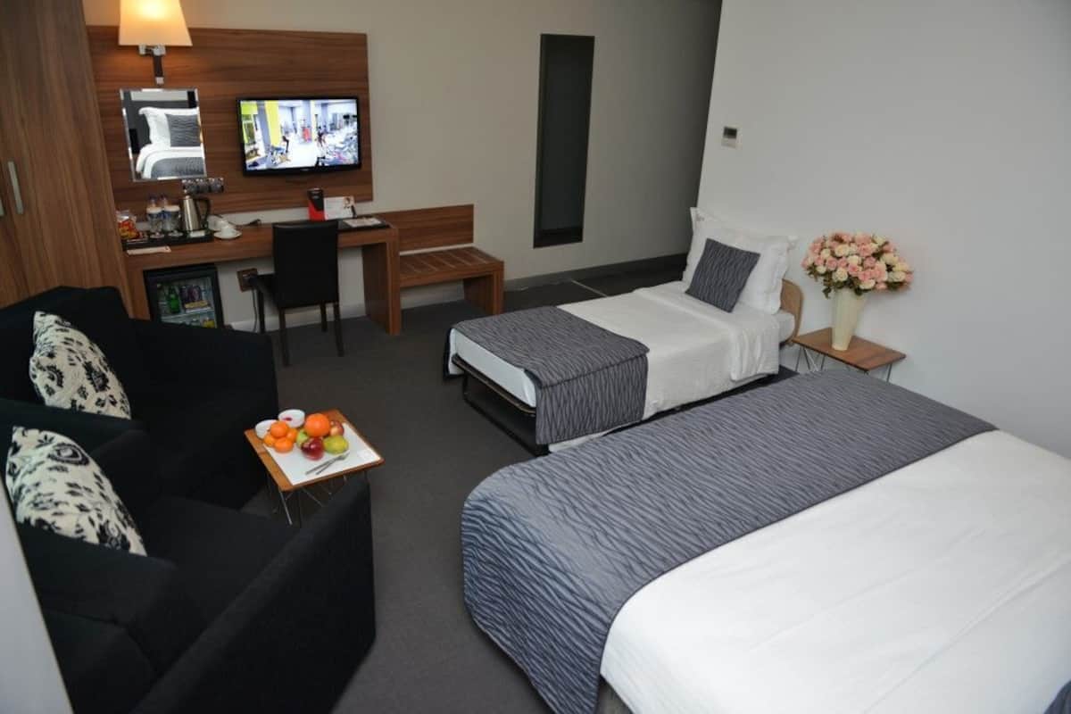 A hotel room with a bed, a desk with a computer, a TV, a small table with fruit, and a couch.