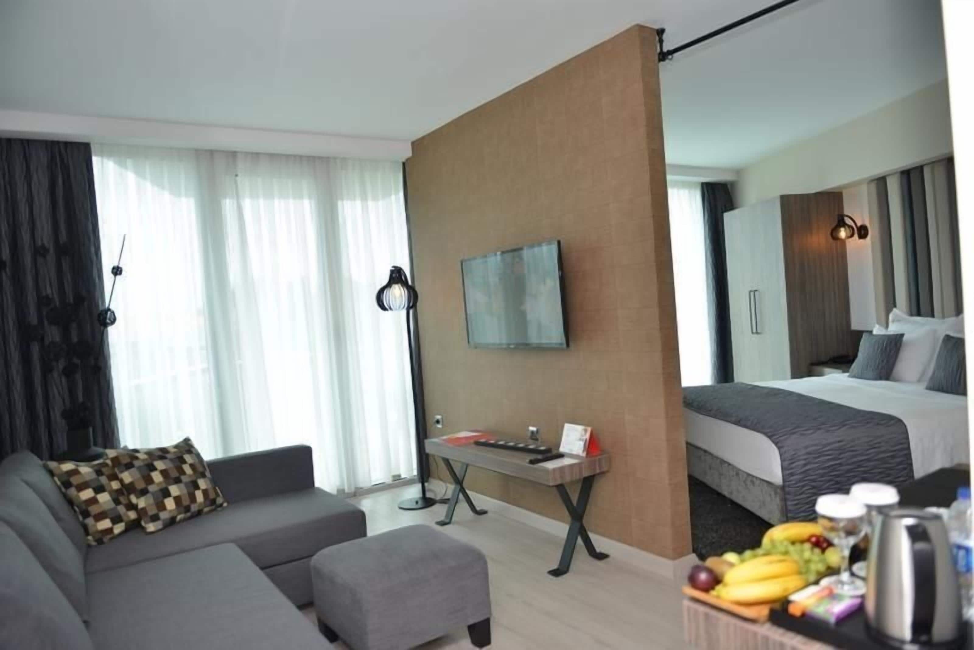 A modern hotel room with a sofa, a small table with a keyboard, a bed, and a breakfast tray with fruits and a coffee maker.