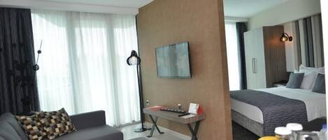 A modern hotel room with a sofa, a small table with a keyboard, a bed, and a breakfast tray with fruits and a coffee maker.