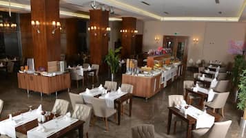 Een ruim restaurant met hoge houten pilaren, meerdere eettafels en stoelen.