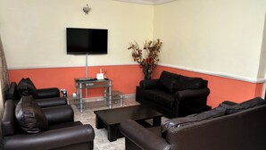 Ein Wohnzimmer mit einem schwarzen Ledersofa, einem Couchtisch und einem an der Wand befestigten Flachbildfernseher.
