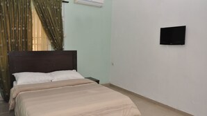 Ein Schlafzimmer mit einem Bett, einem Nachttisch, einem an der Wand befestigten Fernseher und einem Fenster mit Vorhängen.
