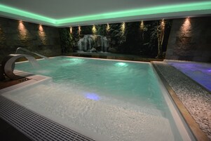 Un área de spa con un jacuzzi, una pared de cascada y un borde revestido de guijarros.