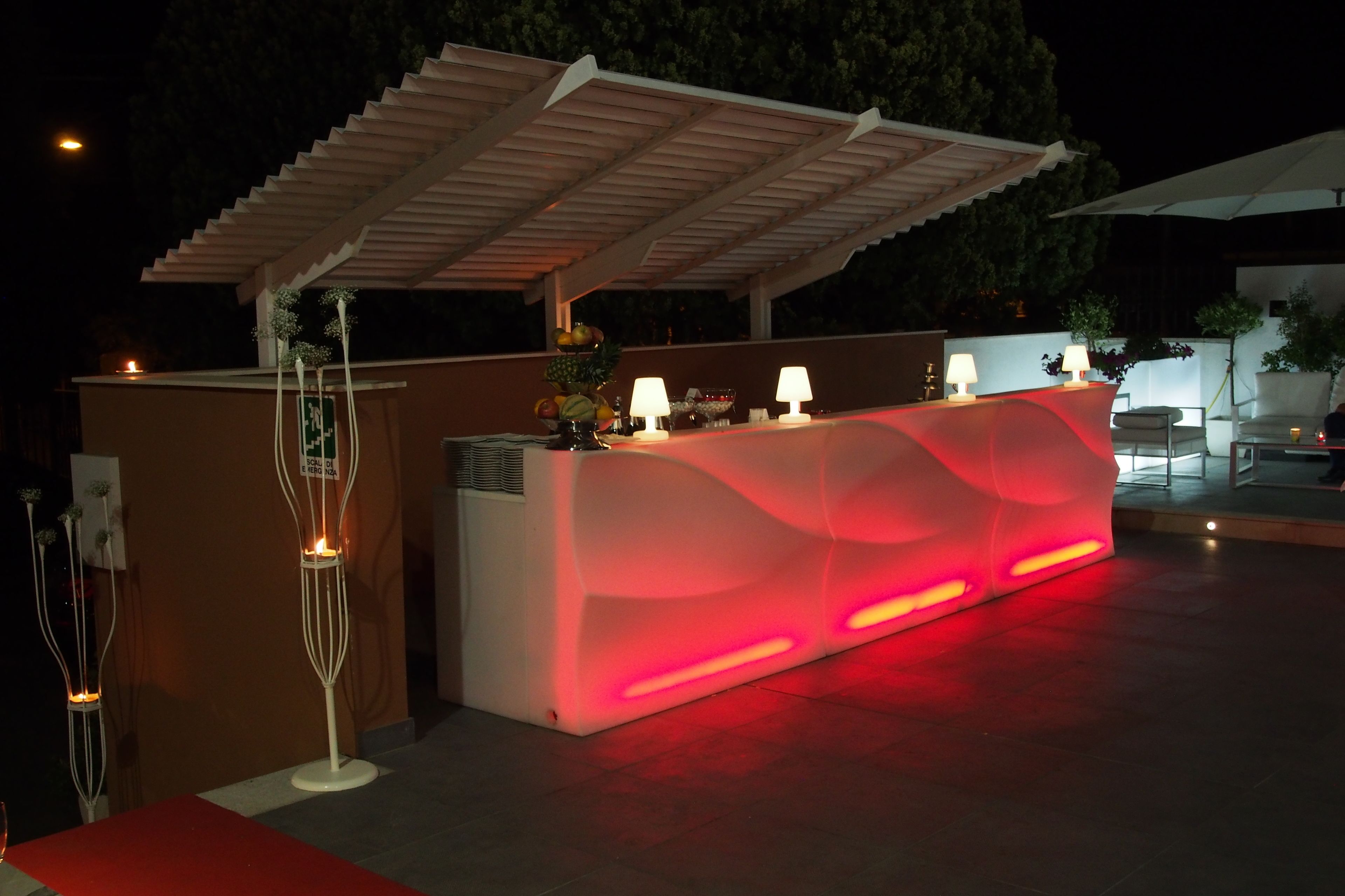 Ein hell erleuchteter Außenbereich zur Rezeption, modern gestaltet, mit einer Theke und einer Sitzgelegenheit unter einer Pergola.