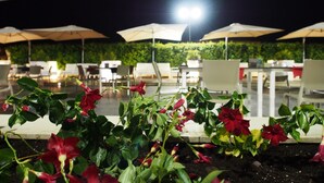 Zona de comedor al aire libre con mesas y sillas bajo sombrillas, rodeada de follaje.