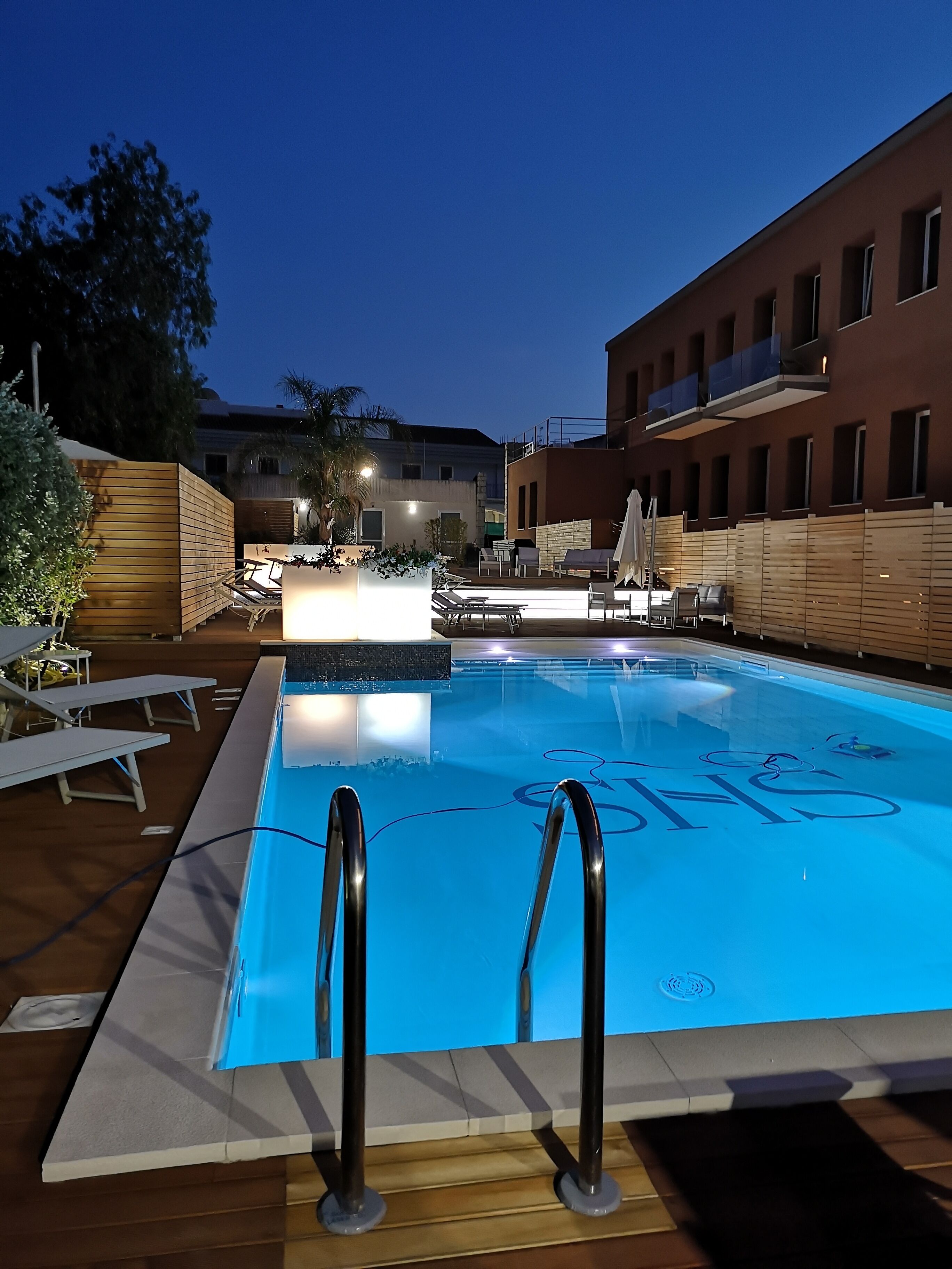 A swimming pool with a blue floor, surrounded by lounge chairs and a wooden deck.