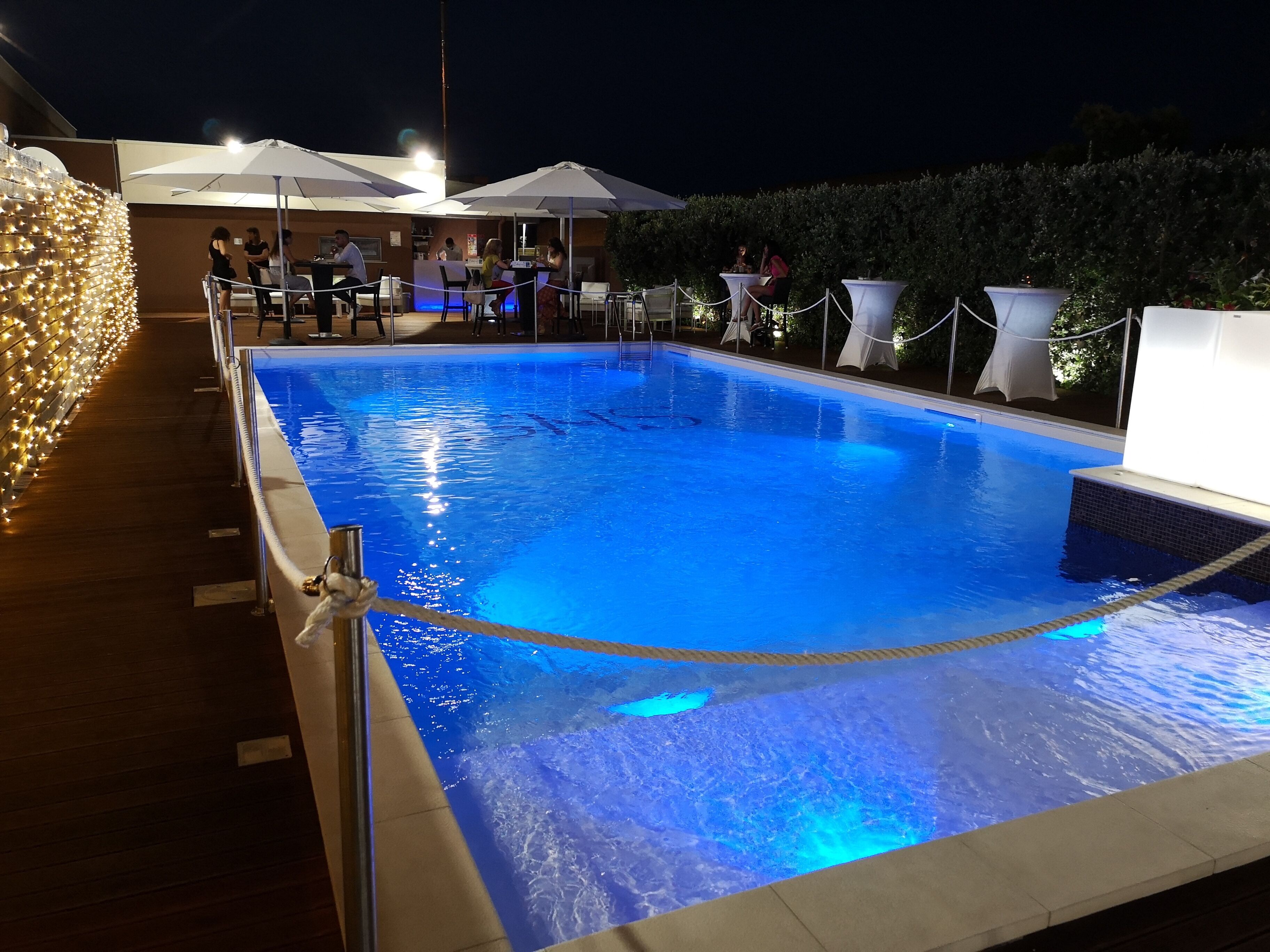Une piscine délimitée par une corde, entourée d’espaces de détente en plein air et de parasols.